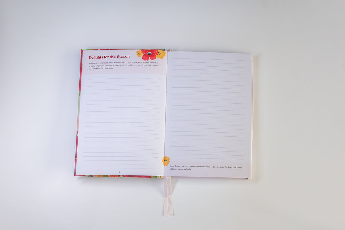 An open lined journal with a floral cover and ribbon bookmark, photographed from above on a plain white background.