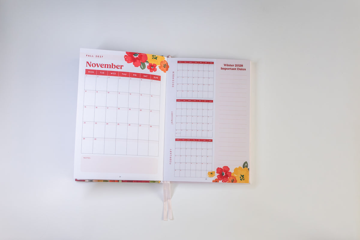 An open planner or calendar showing November and winter 2023 important dates pages, decorated with red and yellow floral illustrations, photographed against a plain white background.