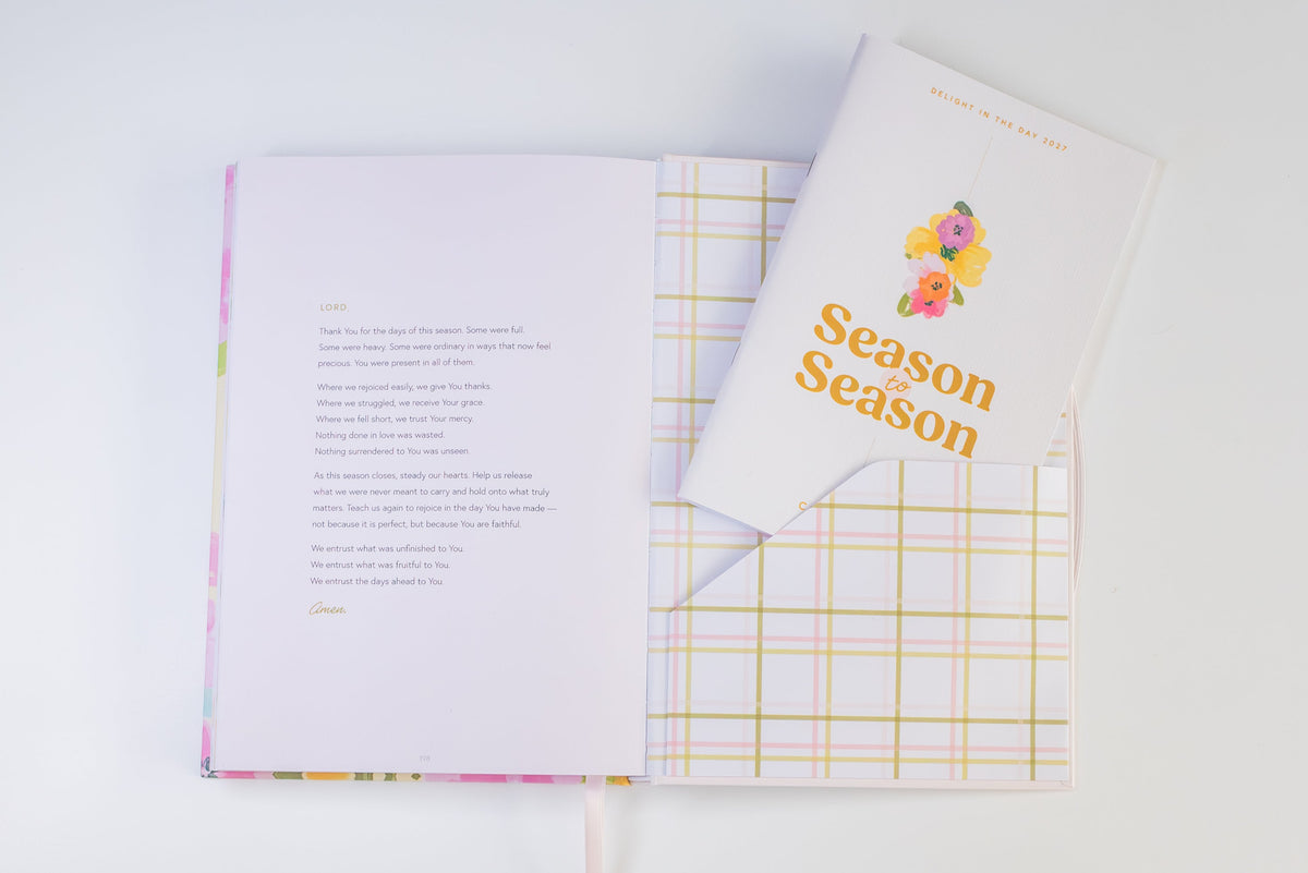 An open journal with printed pages and a matching closed copy labeled 'Season Season' lies on a white background. The journal has a pastel pink cover with a subtle floral border and a yellow-and-white plaid pattern visible on the inside pages.