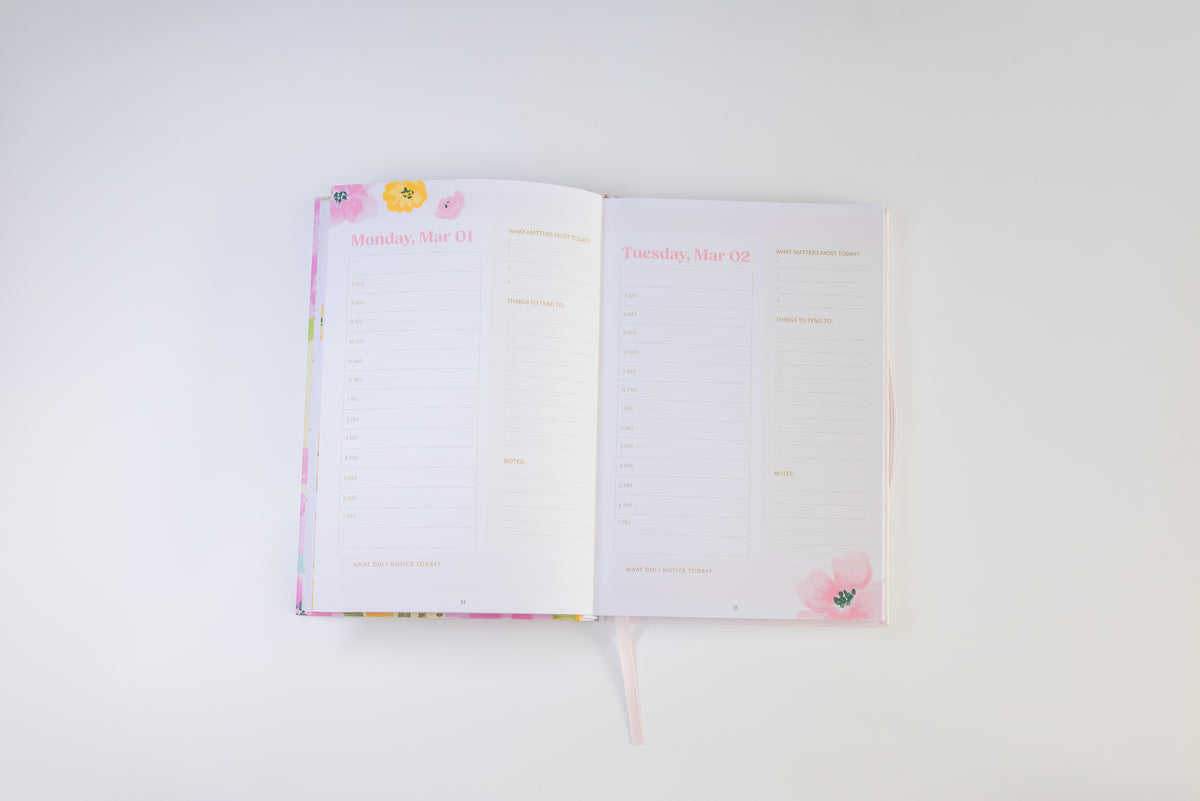 An open planner or agenda with two blank lined pages spread open on a clean white background. The cover and inner pages have a soft pastel floral design with pink, yellow, and green accents.