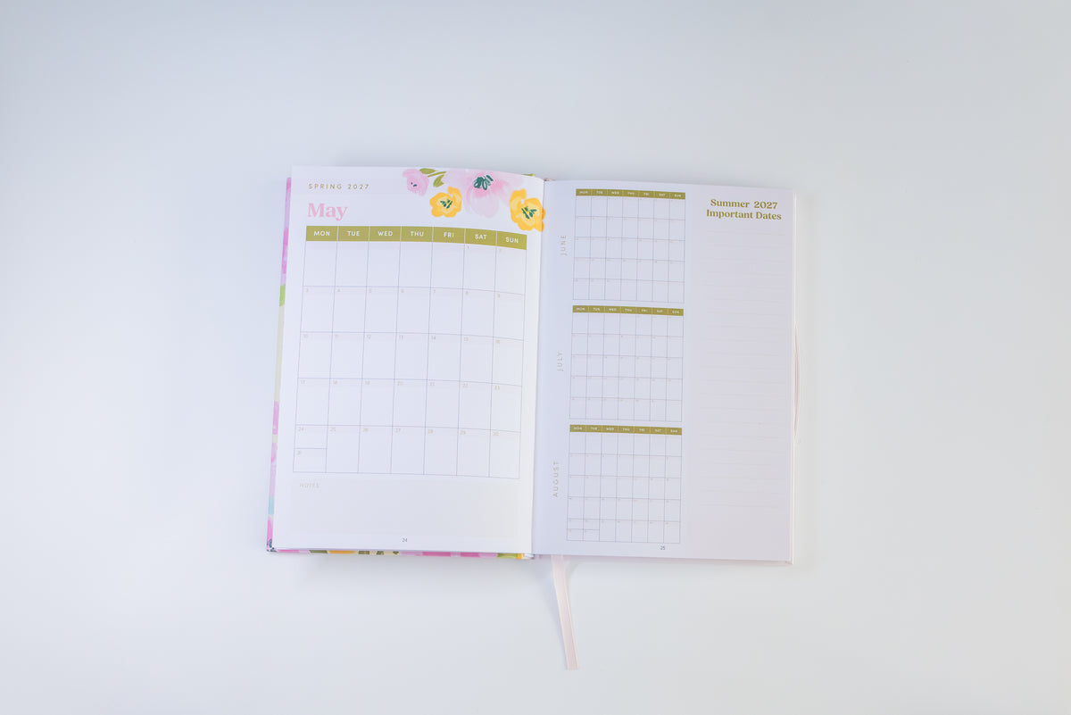 An open planner or calendar showing May 2021 and a weekly schedule page, with pastel floral accents and gold text on a clean white background.