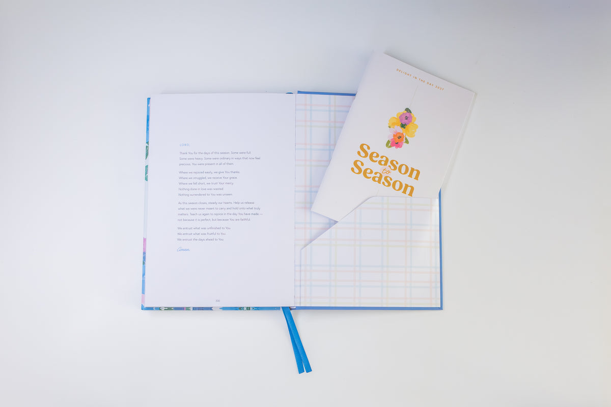 An open notebook or journal with printed text on the left page and a folded cover reading 'Season Season' with small colorful illustrations, placed on a white background.