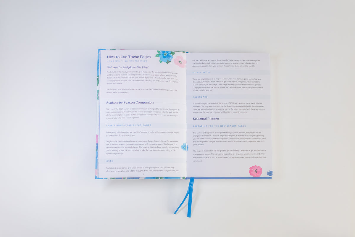 An open instructional booklet or planner with printed pages and a blue ribbon bookmark, photographed from above on a plain white background.