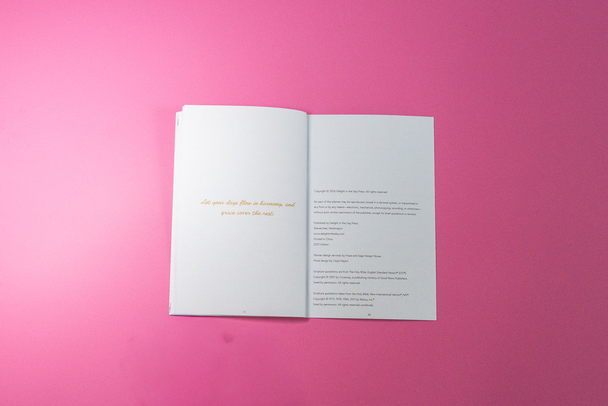 An open book with white pages, featuring a gold quote on the left page and black text on the right page, photographed flat on a vibrant pink background.