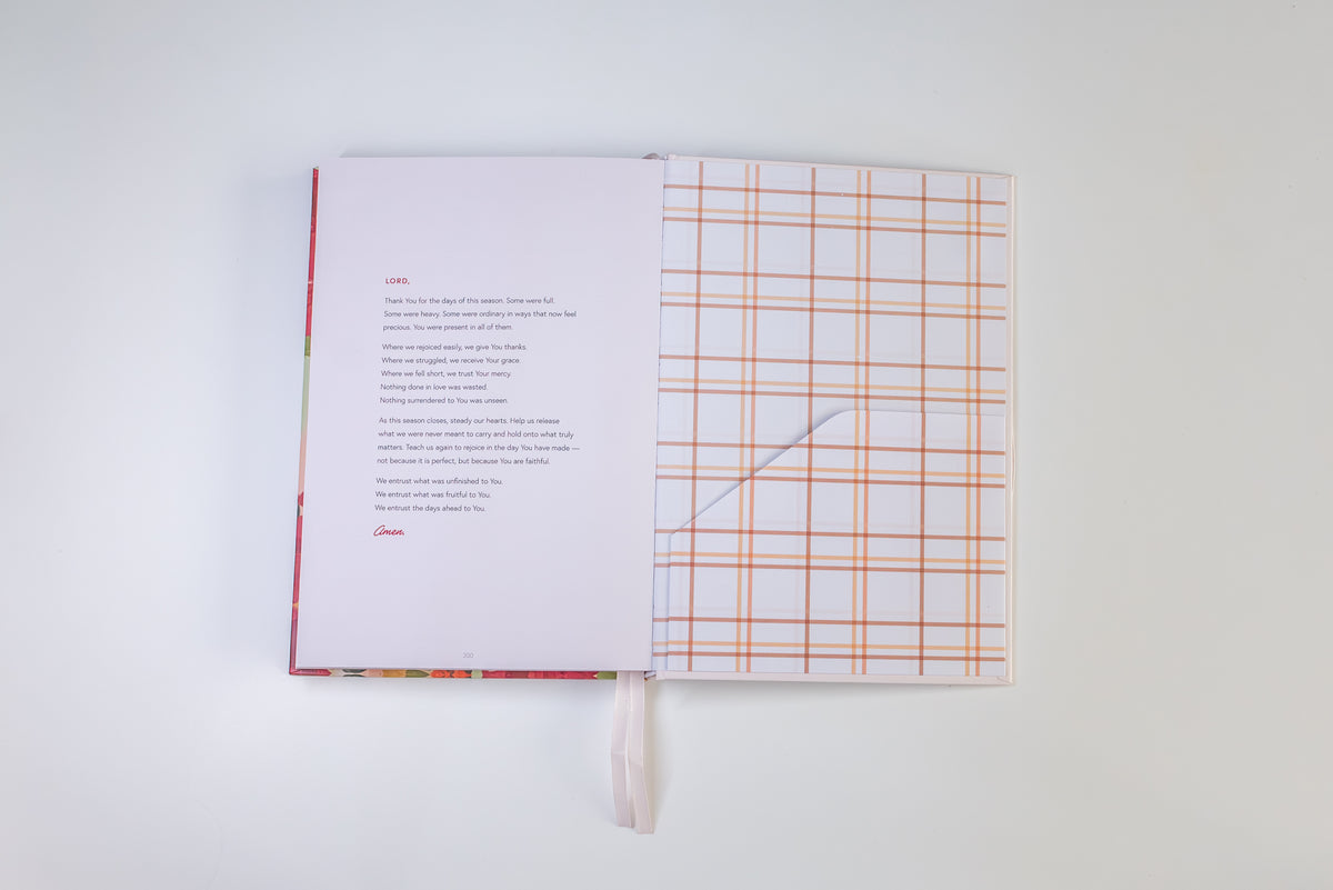 An open book or journal laid flat on a white background, showing printed text on one page and a white page with an orange grid pattern on the other. A white ribbon bookmark hangs from the center.