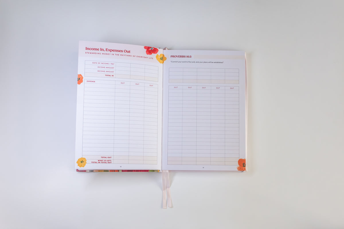 An open planner or notebook showing two interior pages with lined tables and small floral illustrations in orange, red, and yellow, photographed against a plain light background.
