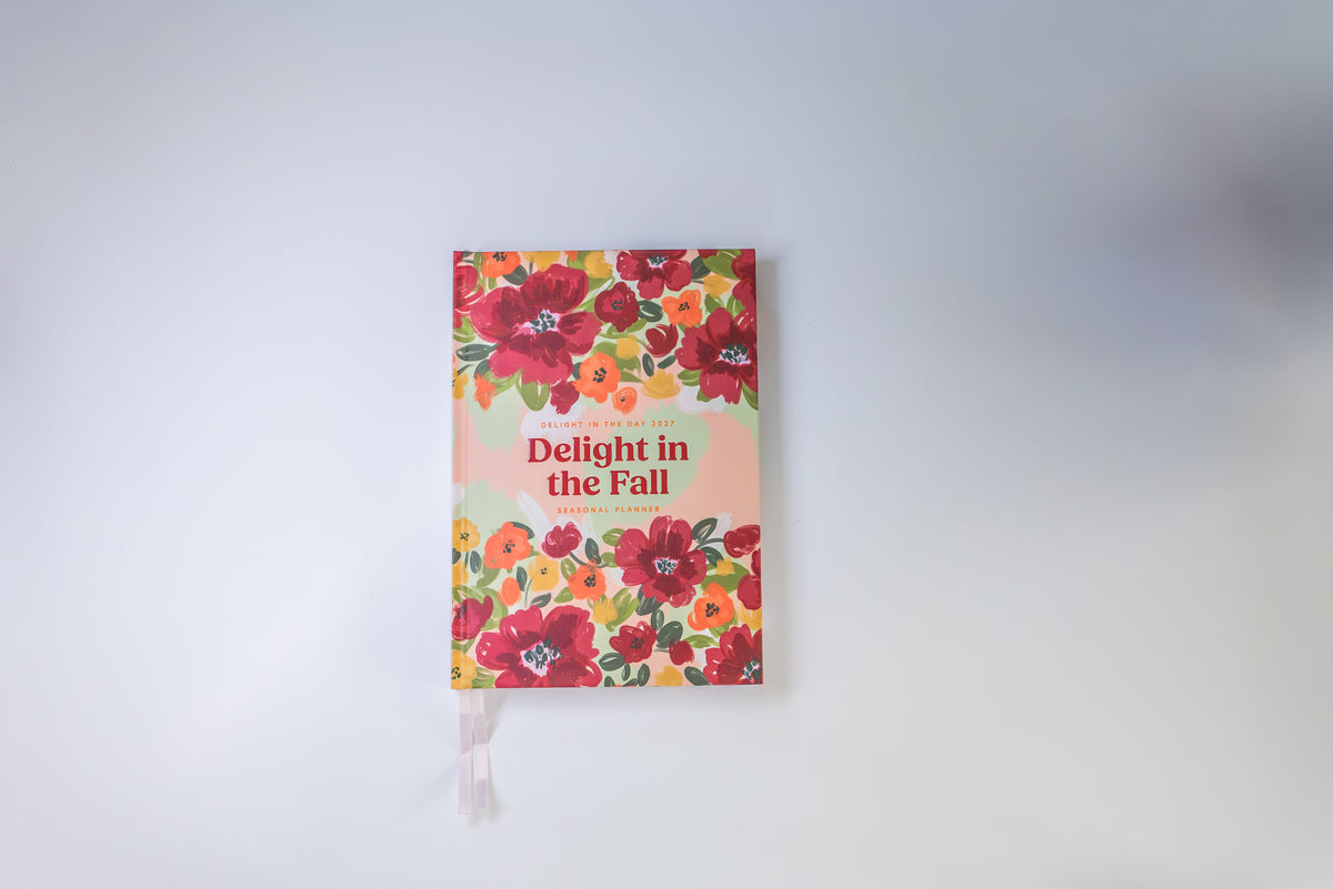 A hardcover journal titled 'Delight in the Fall' by Jane Burrow, featuring a vibrant floral cover with red, orange, and yellow flowers on a light peach background, complete with a white ribbon bookmark.
