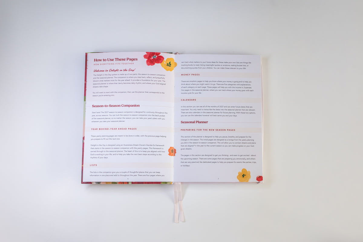An open printed booklet or journal spread laid flat on a light neutral background. The pages contain small text blocks with headings in red and black, decorated with small floral illustrations in red, yellow, and orange.