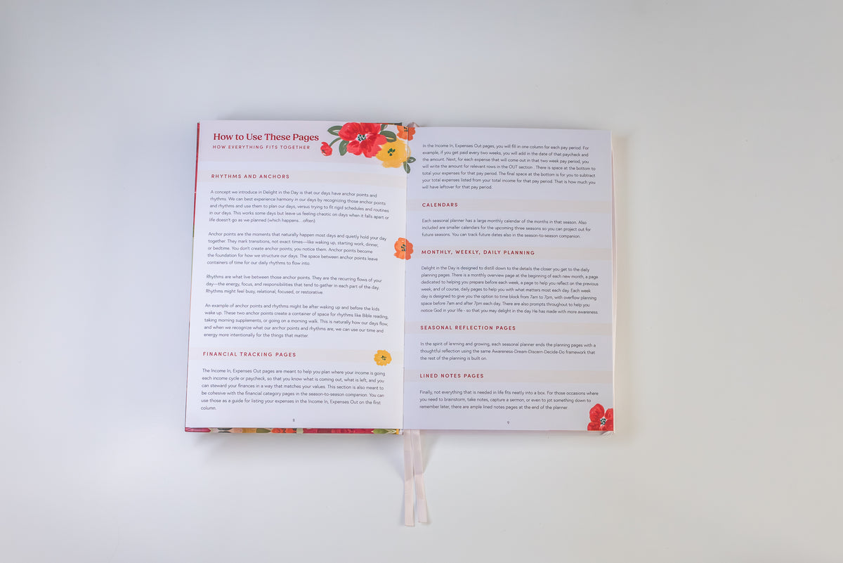An open book or booklet laid flat against a plain white background, showing printed pages with headings, paragraphs of text, and small floral illustrations in red, orange, and yellow near the top and bottom margins.