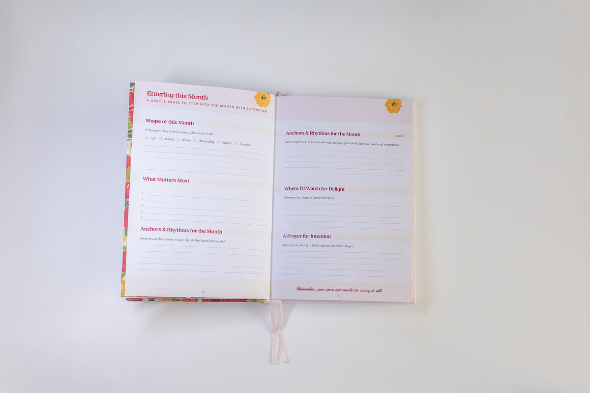 An open printed journal or planner spread on a plain white background, showing lined pages with pink headings and small floral illustrations in the corners.