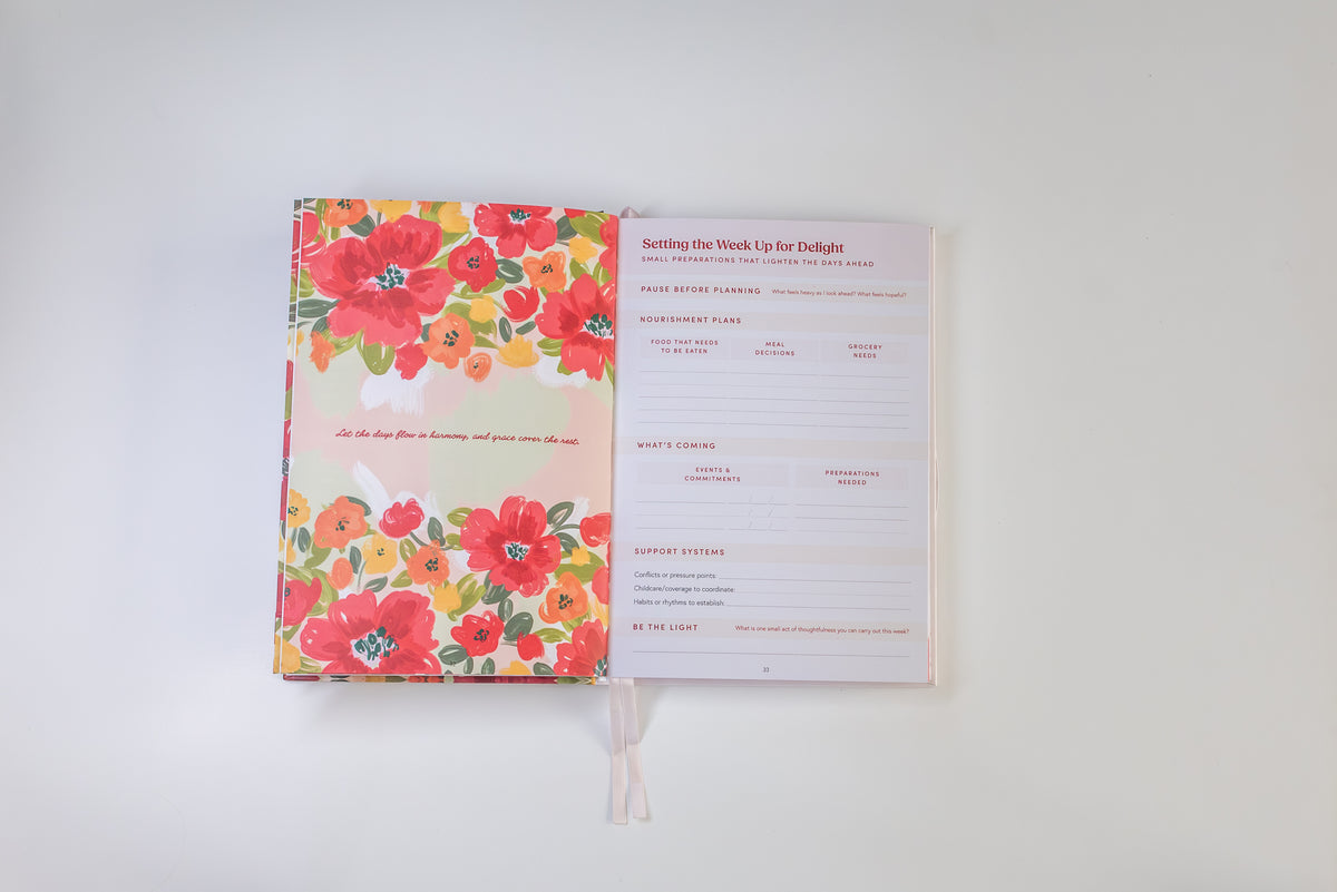 An open planner or notebook with a bright floral cover on the left and printed weekly planning pages on the right, photographed on a clean white background.