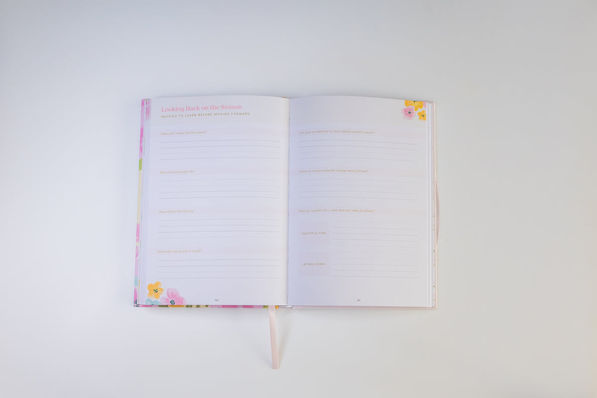 An open lined journal or planner with pastel floral covers and ribbon bookmarks, photographed from above on a plain white background.