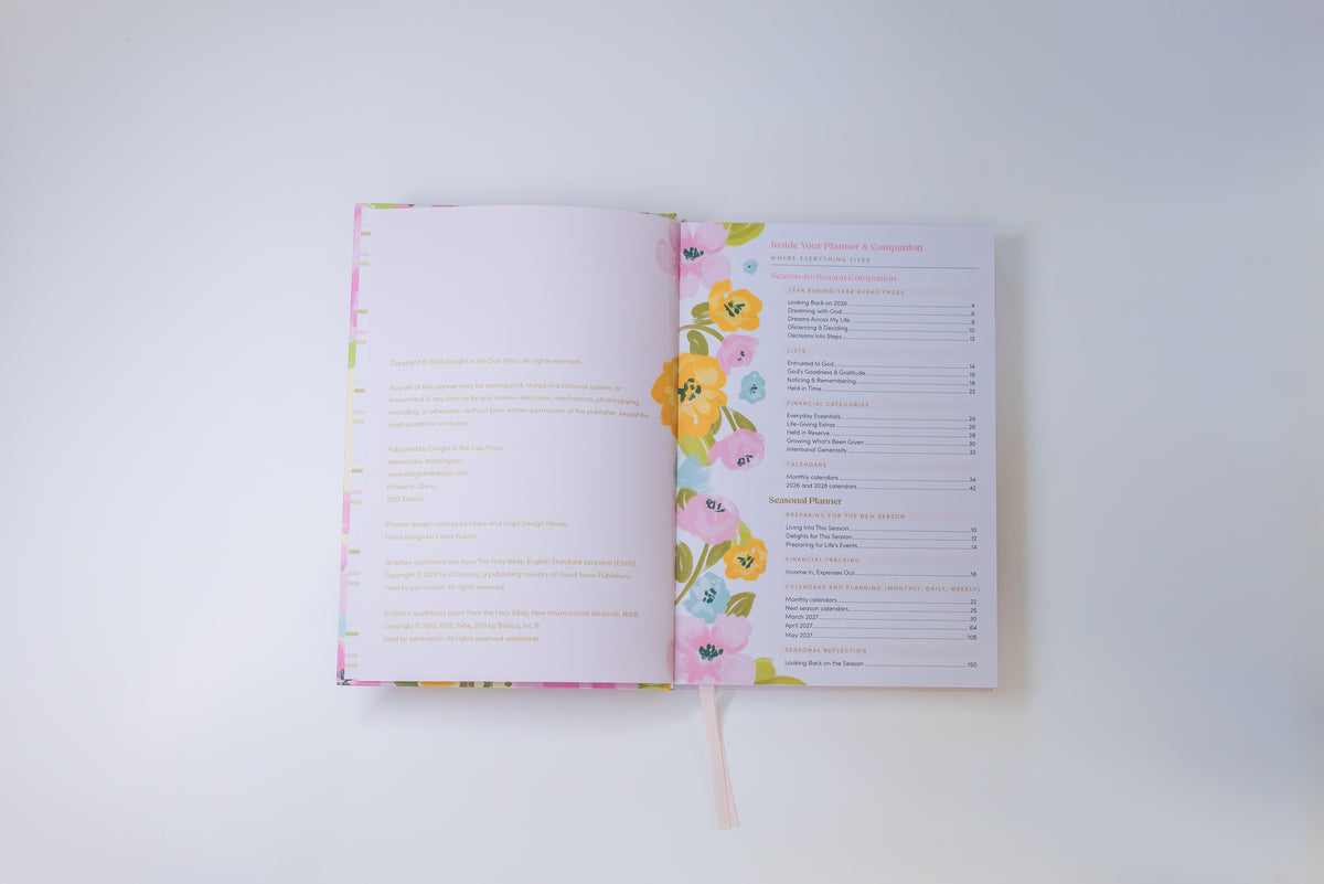 An open recipe book with a pastel floral border on the pages, showing a recipe spread and a colorful index page, photographed from above on a light gray background.