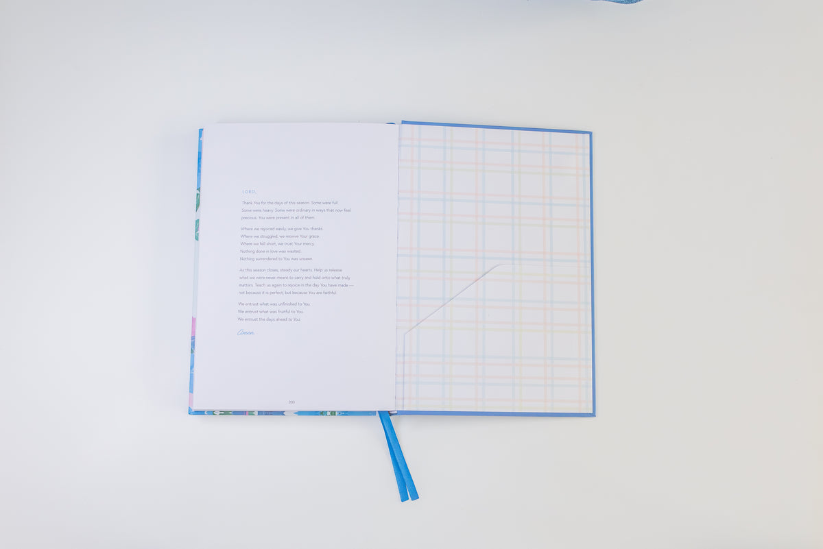 An open notebook or journal with a blue cover and ribbon bookmark, laid flat on a white background. The left page contains printed text, and the right page has a light blue grid pattern.