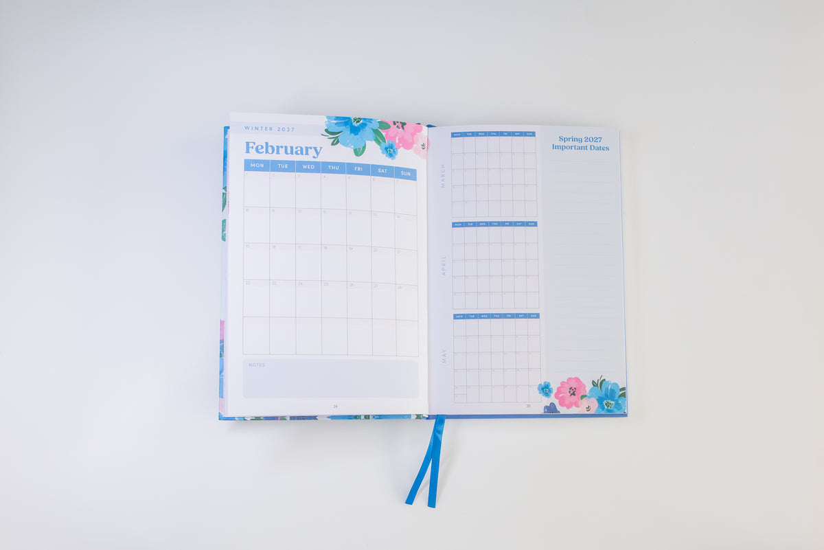 An open planner or agenda with floral cover details and blue ribbon bookmarks, showing February and April 2027 pages on a clean white background.