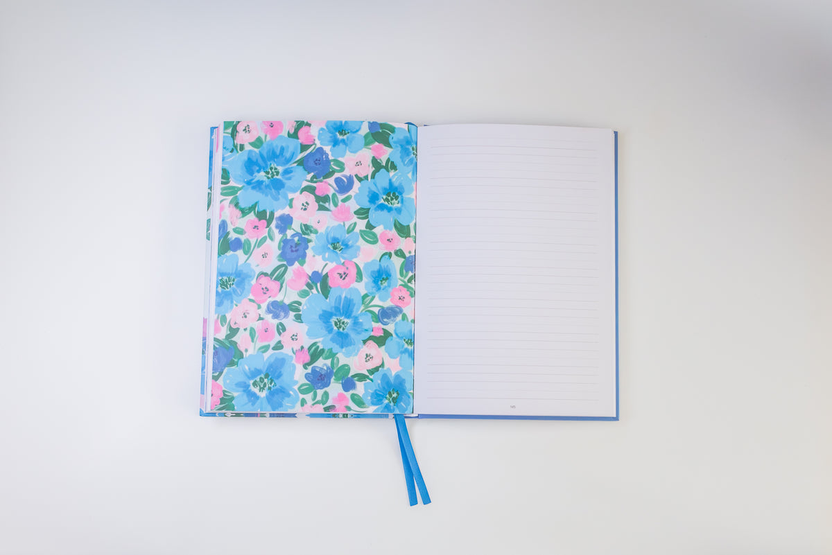 An open notebook with a floral-patterned cover on the left and lined blank pages on the right, photographed from above on a clean white background.