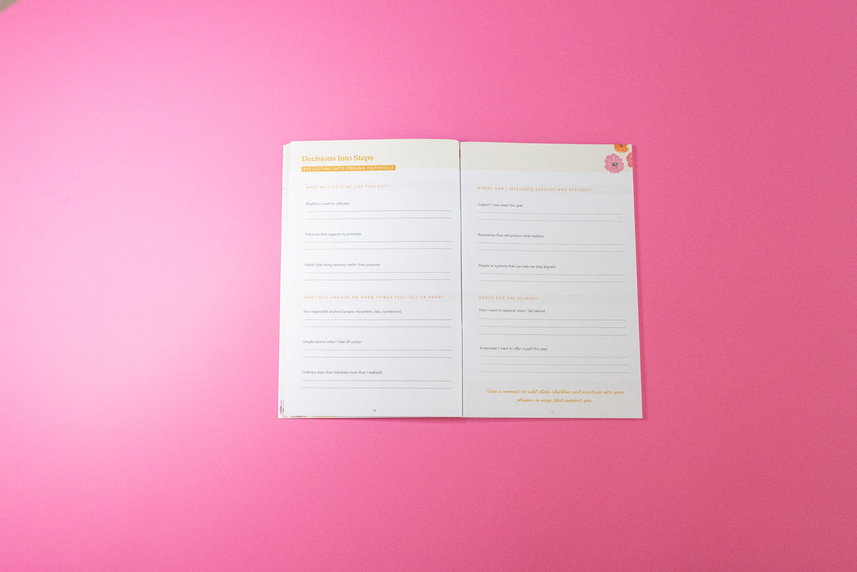 An open booklet or planner showing two printed pages with lined writing areas and small decorative graphics, placed on a solid pink background.