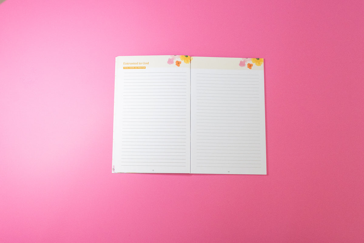 An open two-page lined notepad with small floral accents in the top corners, placed on a solid pink background.