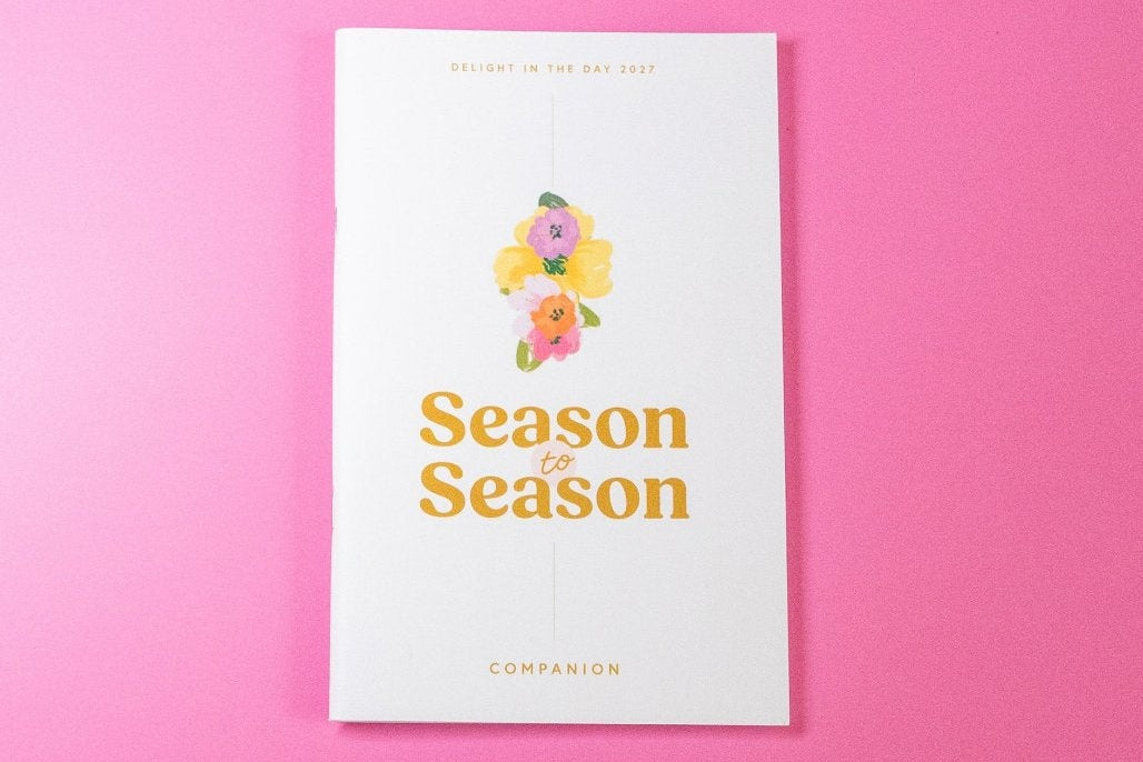 A white booklet or magazine titled 'Season Season' with a colorful illustration and gold lettering, centered on a solid pink background.