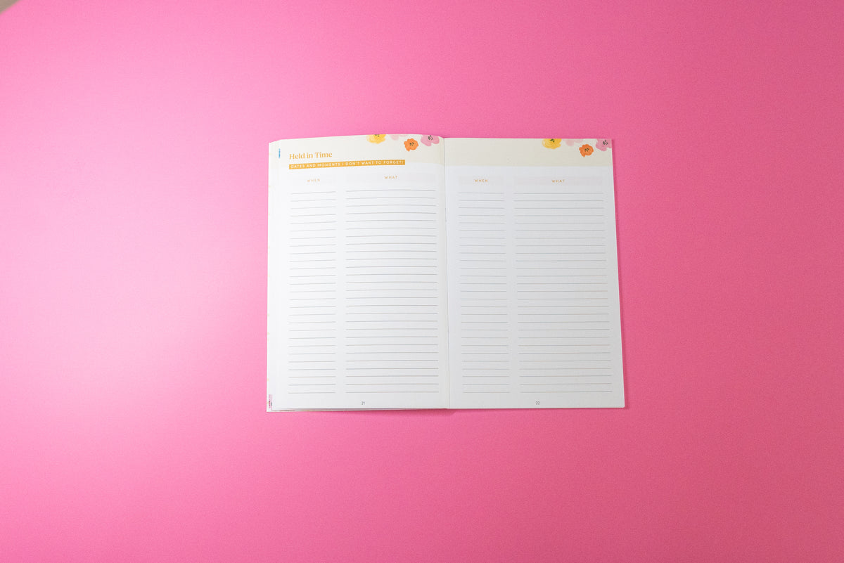 An open white planner insert or notepad with lined writing sections and small floral accents at the top, photographed on a solid pink background.