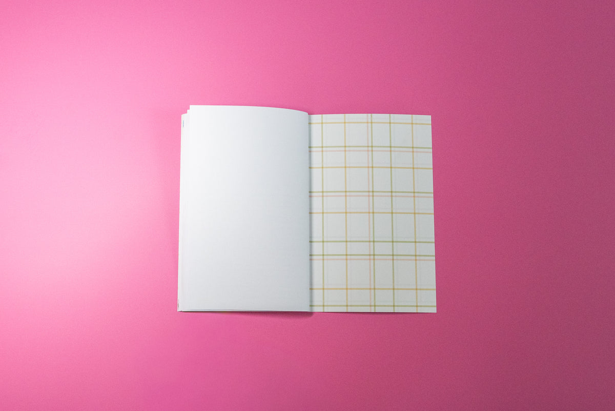 An open notebook or journal with blank white pages on the left and a left-hand page featuring a yellow grid pattern on the right, set against a solid pink background.